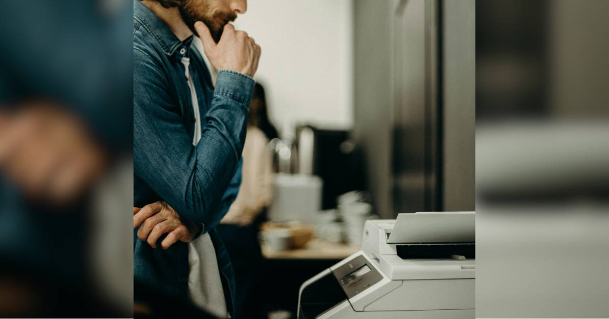 A man looking at a printer copier cosidering what setting to use on the business copier to save money on printing